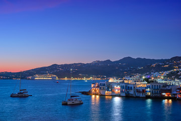 Naklejka na ściany i meble Sunset in Mykonos island, Greece with yachts in the harbor and colorful waterfront houses of Little Venice romantic spot on sunset and cruise ship illuminated in night. Mykonos townd, Greece