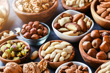 Mixed nuts in wooden bowls on black stone table. Almonds, pistachio, walnuts, cashew, hazelnut. Top view nut photo.