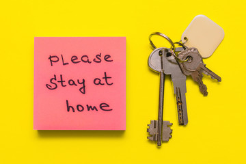 Bunch of keys and pink sticker with the inscription PLEASE STAY AT HOME on a yellow background.Concept of self isolation and home quarantine from Covid-19
