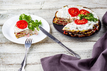 Zucchini cake with tomatoes and fresh parsley on white wooden background.