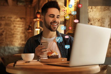 Young blogger with laptop and phone at table in cafe