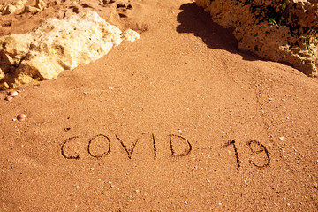 Travel and tourism concept, novel coronavirus 2019-nCoV pandemic alert. COVID-19 text written on the sandy beach in Algarve. The spread of corona virus in the World impact on tourism and holidays.