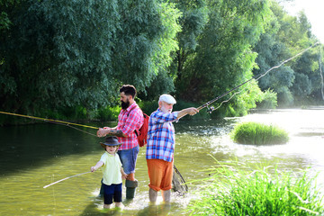 Little boy fly fishing on a lake with his father and grandfather. Man with his son and father on...