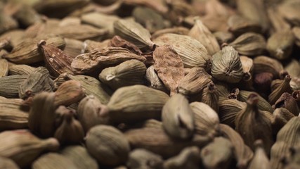 Cinematic passage of the camera over a handful of green raw dry cardamom scattered on the table. Rotating camera over seasoning