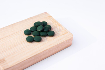 Spirulina tubs on a light brown wooden cutting board. Healthy lifestyle. Place for a text. Closeup.