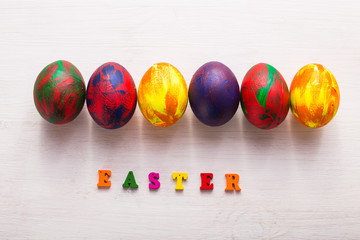Multi-colored wooden letters making up the words happy easter and decorative colourful eggs on a white background with copy space.
