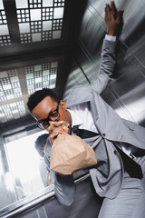 stressed african american businessman breathing with paper bag and suffering from panic attack in...