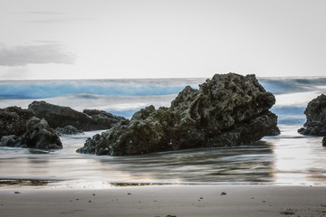 Fototapeta na wymiar Long Exposure Shot of Rocks on a Beach with Ocean Waves during Daylight