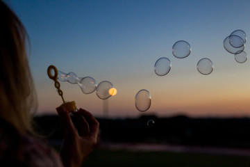 Girl blowing soap bubble sunset party 