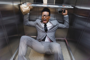 scared screaming african american businessman with smartphone and paper bag suffering from panic attack in elevator © LIGHTFIELD STUDIOS
