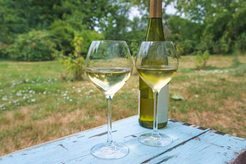 Two glasses and bottle of white wine on old blue paint table in the summer garden