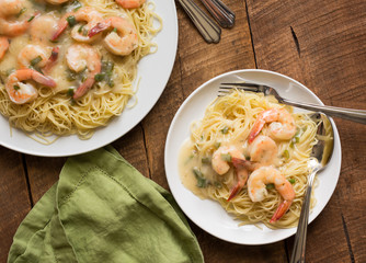 Top view of angel hair pasta with shrimp, set on a rustic wood table with white dinnerware. 