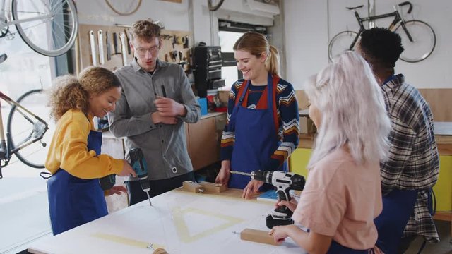 Multi-cultural team of trainees in workshop learning how to assemble hand built bicycle frame using electric drill - shot in slow motion