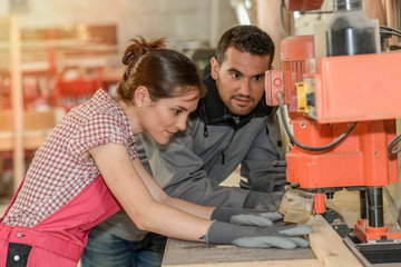 Male worker teaching female apprentice how to operate a machine