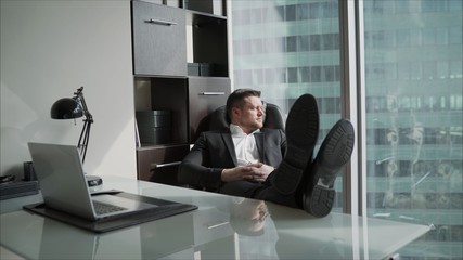 Businessman in his office throws legs on the table. An exhausted businessman sits with legs on his table and plays with crumpled paper balls. 4K.