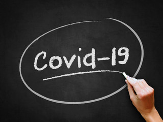 A hand writing 'Covid-19' for health and social issues on Coronavirus (Covid-19) concept design.