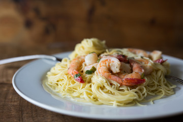 Shrimp and angel hair pasta on a white plate. Close up view, wood background. Copy space. 