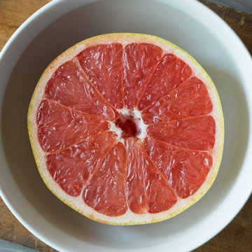 Half Of A Pink Grapefruit In A White Bowl. Overhead Shot. 