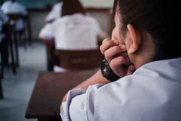 School students taking exam writing answer in classroom with stress..