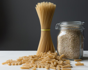 Brown rice pasta and brown rice grains in a jar. Roomy for copy, gray background. 
