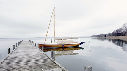 Sailing Boat docking on a pier at a lake with calm water reflection on a grey and cloudy day