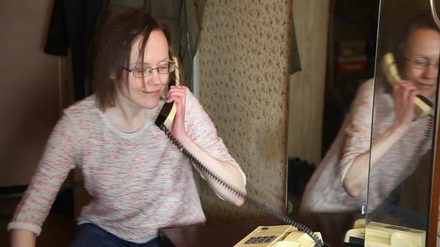 Woman is speaking on retro soviet phone, sitting near mirror. Reflection of woman.   Old soviet flat ret