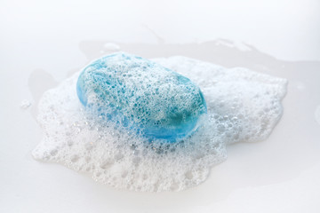 bar of blue soap with a lot of foam and bubbles on a white background, health care and hygiene concept against coronavirus infection, copy space