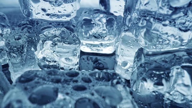Melted ice cubes close up. Camera moves through ice cubes with water drops over dark background. UHD, 4K
