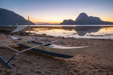 El Nido, Palawan, Philippines. Traditional fishing banca boat on shore. Cadlao Island in sunset light in background. Vacation season