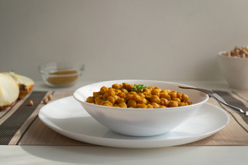 Braised chickpeas with onions and curry in a white plate on a light background. Vegetarian food. Healthy eating