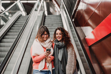 two friends waiting going down stairs at the station before catching a train. Using mobile phone. Travel photography. Lifestyle.