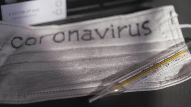 Coronavirus. Medical disposable gauze bandages are on the table. A mercury glass thermometer rests on a protective medical mask.
