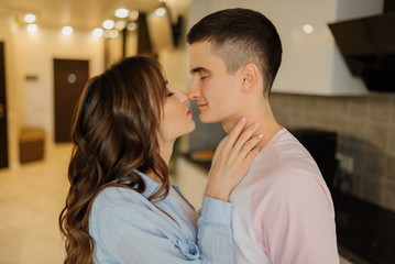 Loving couple stand in the kitchen with their eyes closed, touch each other with their noses while standing on light modern kitchen. Relationship concept.