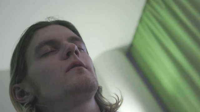 Young man with closed eyes and sick look. Stock. Angled view of man with closed eyes and feeling dizzy or lost in thought. Effect of vertigo or hypnosis on young man