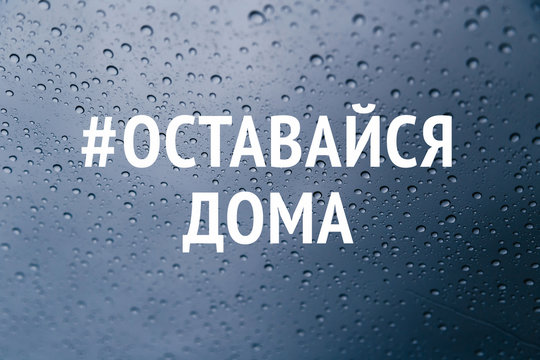 Stay at home in russian language social media campaign for coronavirus prevention. Stay home stay safe concept. Close up of rain drops on the window at background