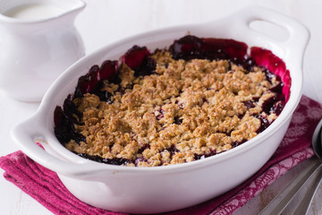 Berry crumble in white baking dish on white wooden background.