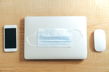 Mask over a laptop and mousse and smartphone over wood table
