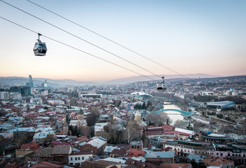 Cable car chair cabins with panoramic sunset view of Tbilisi sights in the background. Tourist attractions  in capital of Georgia.2020