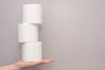 Male hand holding a tower made of three white toilet paper rolls against the gray wall in bathroom