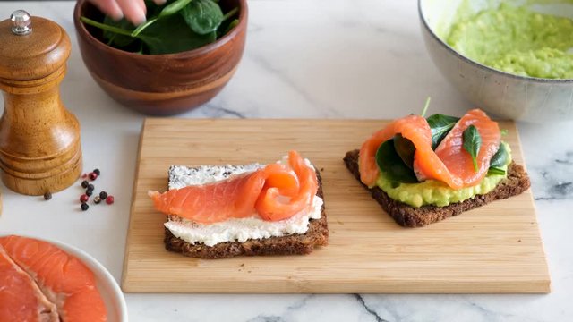 Making a sandwich with cream cheese, smoked salmon and spinach. Healthy rye bread sandwich or toast with fish. Rich in omega 3 snack, appetizer or breakfast