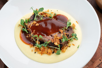 Roast beef with mashed potatoes with barbecue sauce on a plate on a wooden background, close up