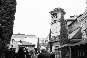Tourists are standing and taking a photographs of the old clock tower and angel hitting the bell  at 2 pm. Things to do in Tbilisi. Georgia .2020