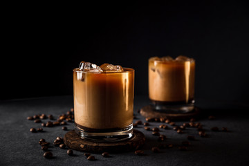 A horizontal photo of 2 rocks glasses with cold iced coffee with milk, coffee beans around, dark...