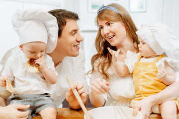 Young caring parents charming mom and cheerful dad keep their cheerful children dressed as cooks and enjoy the results of joint baking. Concept of teaching children home care