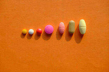 color pills spilling on orange background, top view