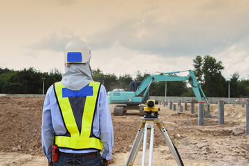Young engineer using camera of surveyor working under the construction site