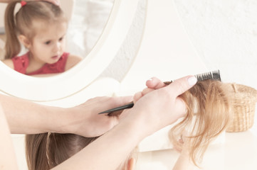 Fototapeta premium hands of mother combing a little smiling girl