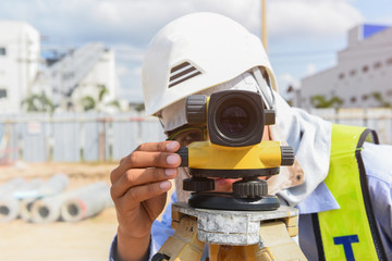 Young engineer using camera of surveyor working under the construction site