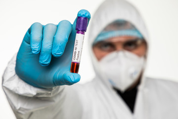 Virologist in a medical mask and protective clothing holds a test tube with positive blood sample...