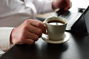 Freelancer is drinking coffee. Concept:  remote work. Hands and laptop closeup.